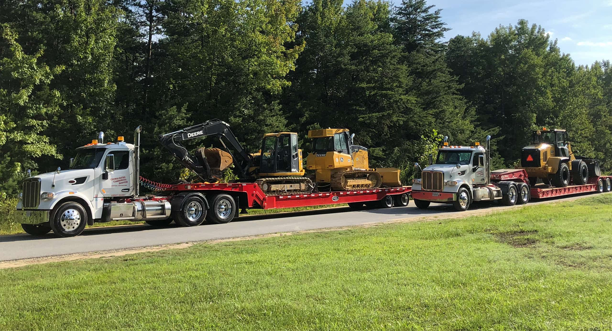 Two large flat-bed trucks carrying heavy equipment